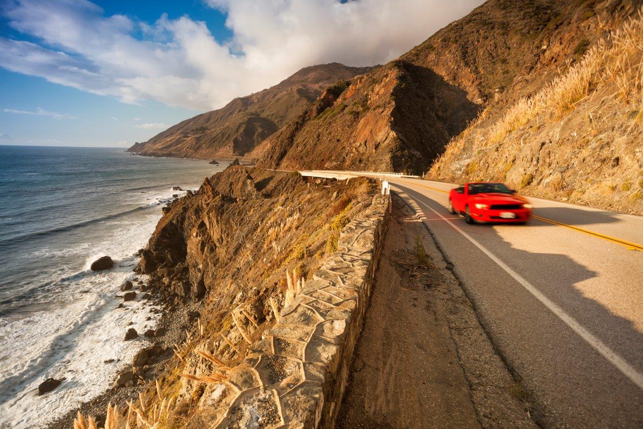 red car driving along the coast